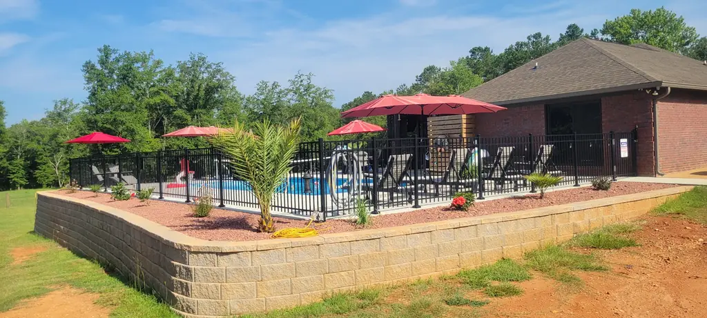 Fenced pool with red umbrellas, a block retaining wall and red clay slope