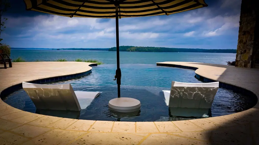 In-water loungers on an infinity-edge pool looking out over a wide lake under an umbrella