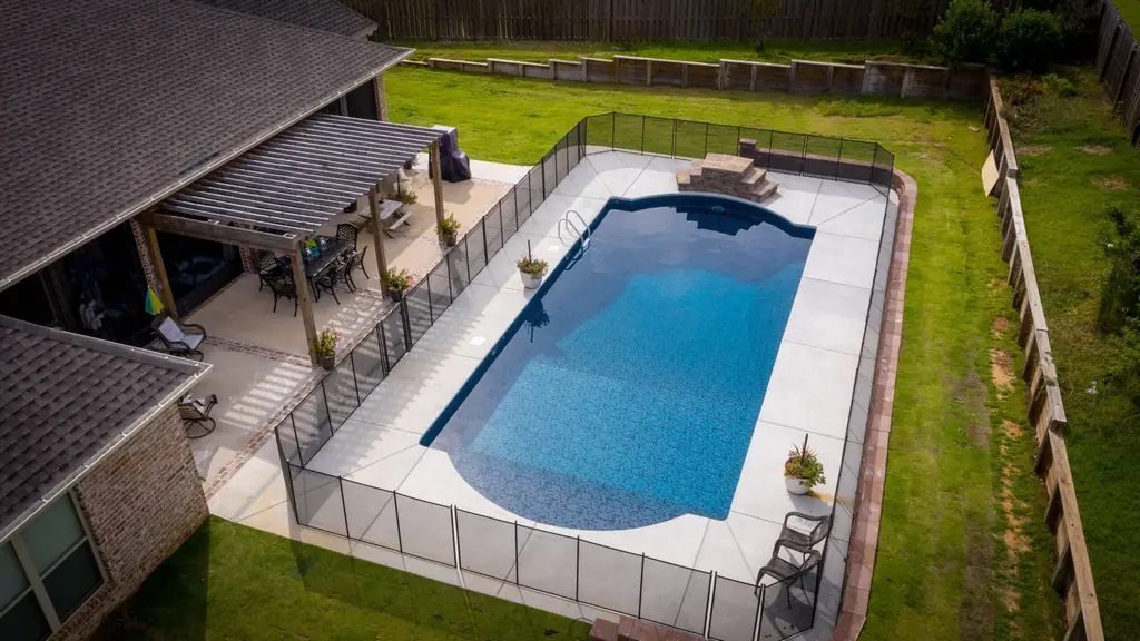 Long rectangular pool in a fenced yard with a patio and a pergola