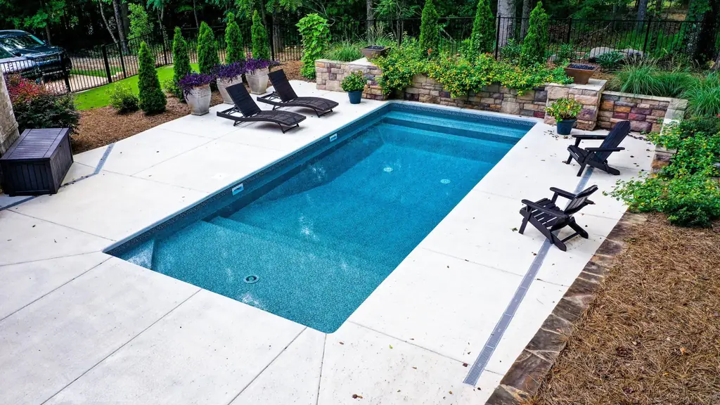 Long rectangular pool with a planted stone wall, outdoor chairs and a gated yard