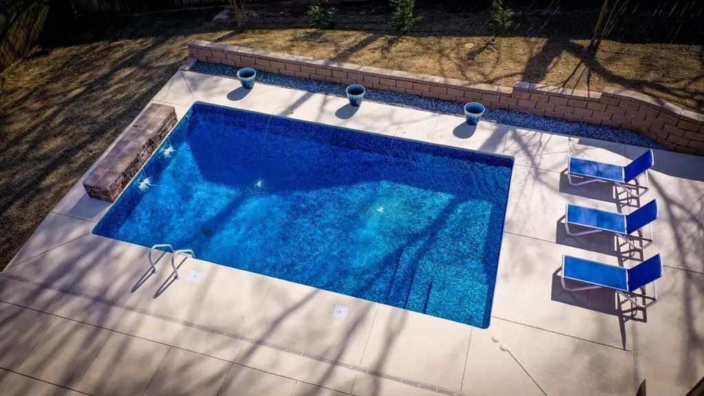 Rectangular pool with a patterned blue liner, a stone ledge and three blue loungers on the deck